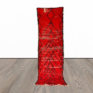 Op de afbeelding: Een rood en zwart loperkleed met een ruitpatroon. Het kleed is gemaakt van wol en heeft een handgeweven textuur.