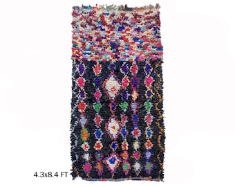May include: A colorful Moroccan rug with a black background and a diamond pattern. The rug is 4.3 x 8.4 feet.