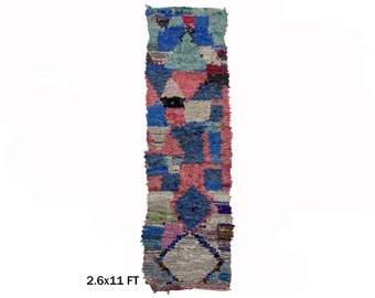 May include: A long, narrow rug with a geometric pattern in shades of blue, pink, and white. The rug is 2.6 feet wide and 11 feet long.