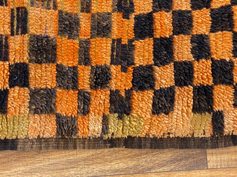 May include: Close-up of a woven rug with a checkered pattern in orange and black. The rug has a thick, fuzzy texture.
