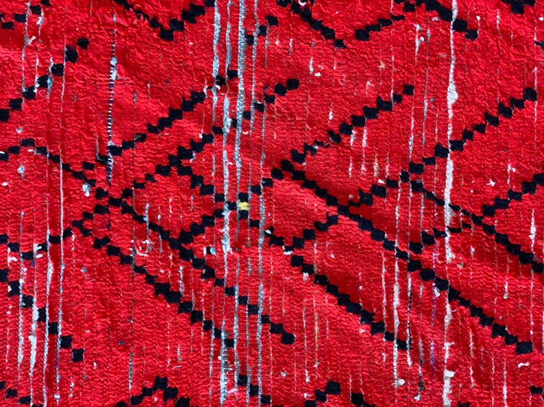 Op de afbeelding: Rode en zwarte geweven stof met een geometrisch patroon. De stof heeft een verweerde look met witte en grijze strepen.