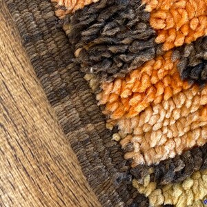 May include: Close-up of a brown, orange, and beige shag rug with a textured border. The rug has a geometric pattern.