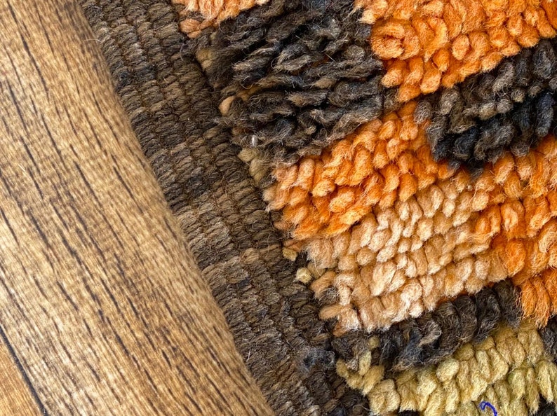 May include: Close-up of a brown, orange, and beige shag rug with a textured border. The rug has a geometric pattern.