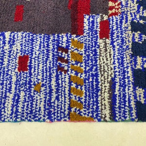 May include: A close-up of a colorful Moroccan rug with blue, white, red, brown, and gold geometric patterns. The rug has a thick, textured pile.