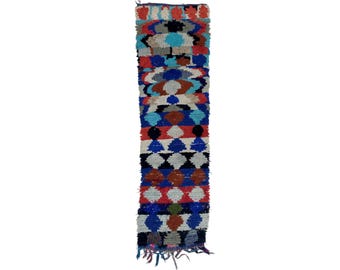 May include: A long, narrow rug with a geometric pattern in shades of blue, red, white, and black. The rug has a fringe on the bottom.