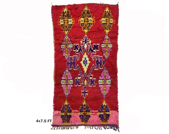 May include: A red Moroccan rug with a geometric pattern in shades of purple, pink, yellow, and white. The rug is 4x7.5 feet.