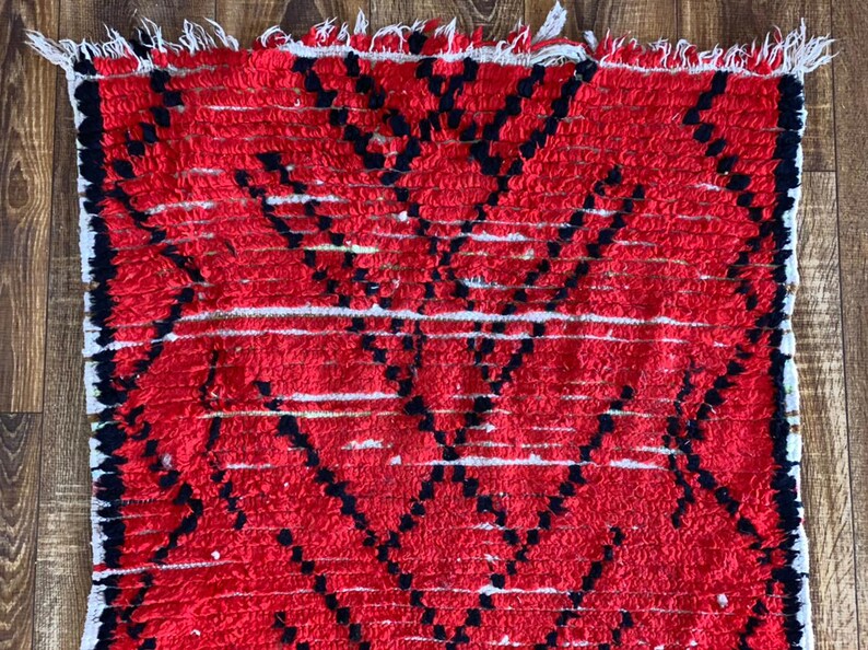 Op de afbeelding: Rood en zwart gestreept tapijt met een gefranst randje. Het tapijt heeft een geometrisch ontwerp met een witte achtergrond.