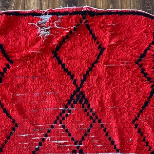 Op de afbeelding: Een rood Marokkaans tapijt met een zwart ruitpatroon. Het tapijt heeft een verweerde, vintage uitstraling en is gemaakt van wol.