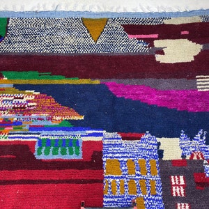 May include: A colorful Moroccan rug with geometric patterns in shades of blue, red, green, yellow, and white. The rug has a fringed edge and is made of wool.
