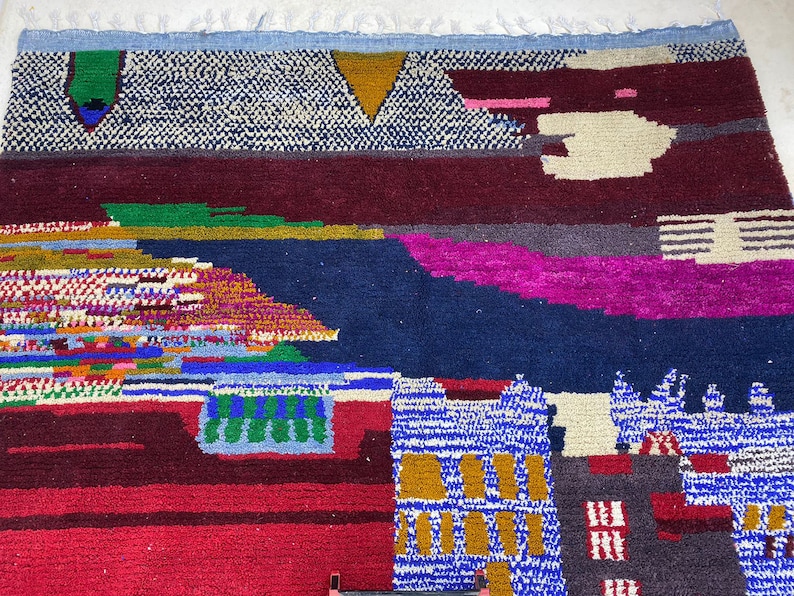 May include: A colorful Moroccan rug with geometric patterns in shades of blue, red, green, yellow, and white. The rug has a fringed edge and is made of wool.