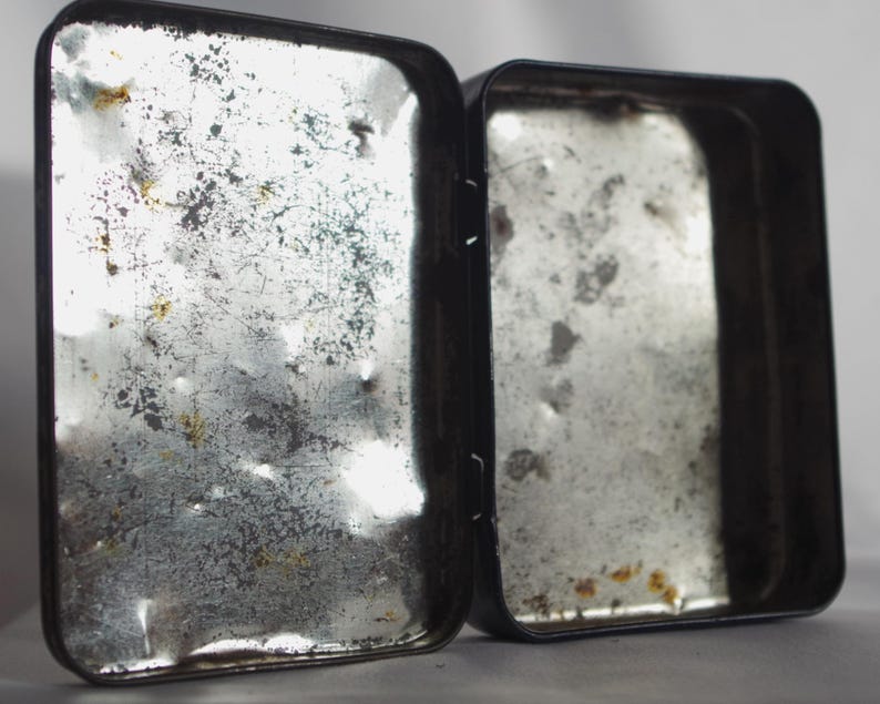 May include: Two empty metal tins with a worn, silver finish. The tins are rectangular and have a hinged lid.