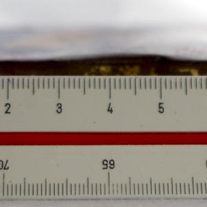 May include: A close-up of a ruler measuring a rectangular object with a gold-colored surface. The object is approximately 7 inches long.