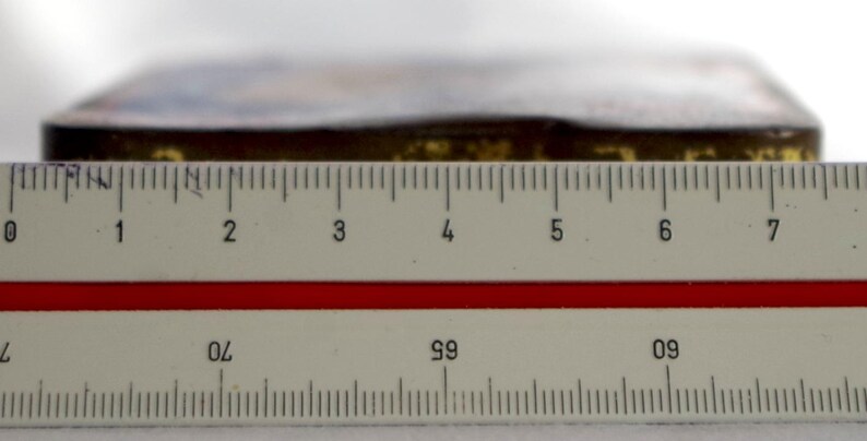 May include: A close-up of a ruler measuring a rectangular object with a gold-colored surface. The object is approximately 7 inches long.