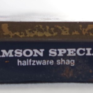 May include: A blue tin with a gold top and the text "SAMSON SPECIAL halfzware shag" printed on the front.