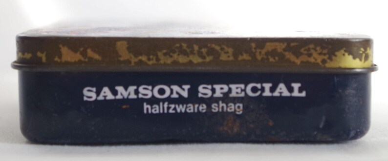May include: A blue tin with a gold top and the text "SAMSON SPECIAL halfzware shag" printed on the front.