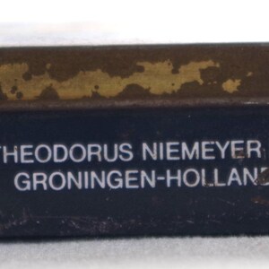May include: A blue metal tin with a gold lid. The tin has the text "THEODORUS NIEMEYER BV. GRONINGEN-HOLLAND" printed on the front.