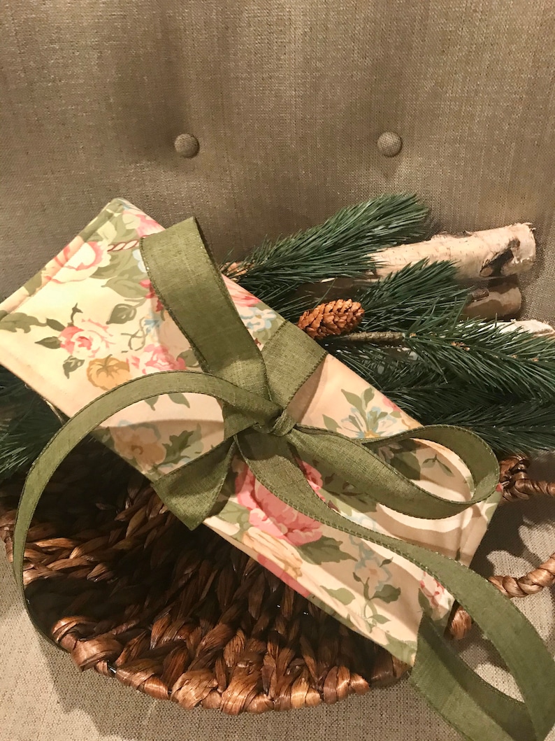 May include: A floral fabric gift bag with a green ribbon tied around it. The bag is sitting in a brown wicker basket.