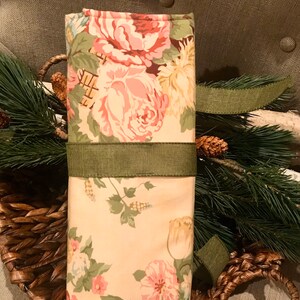 May include: A floral fabric gift wrap with a green ribbon tied around it. The fabric features a white background with pink and green roses.