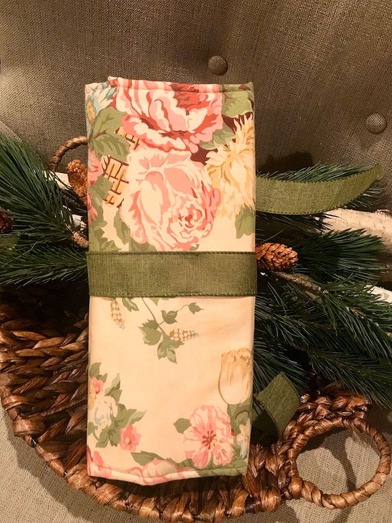 May include: A floral fabric gift wrap with a green ribbon tied around it. The fabric features a white background with pink and green roses.
