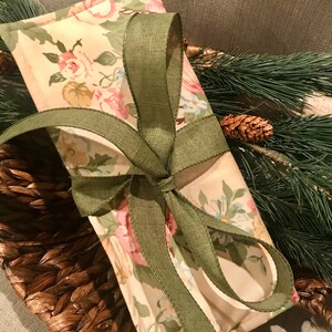 May include: A small gift bag with a floral print and a green ribbon tied in a bow. The bag is sitting on a woven basket.