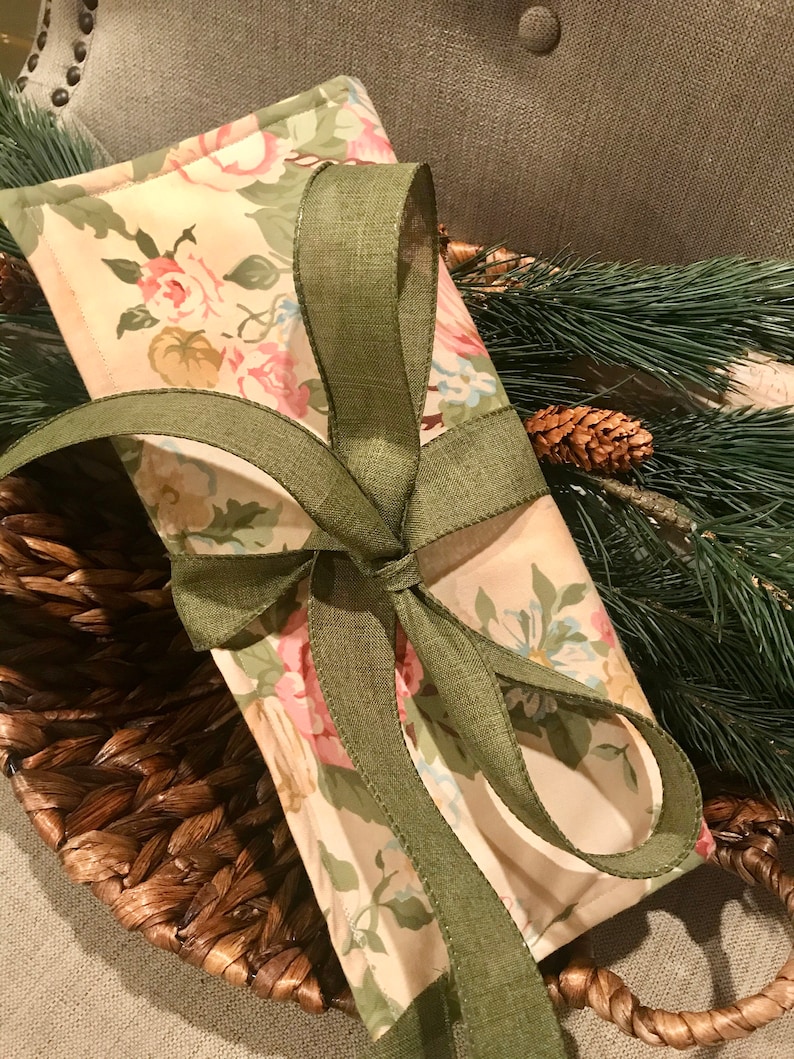 May include: A small gift bag with a floral print and a green ribbon tied in a bow. The bag is sitting on a woven basket.