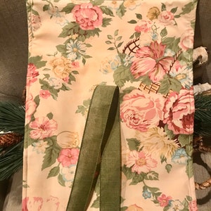 May include: A beige fabric tote bag with a floral print and green fabric straps. The bag is lined with a cream fabric and has a floral print.
