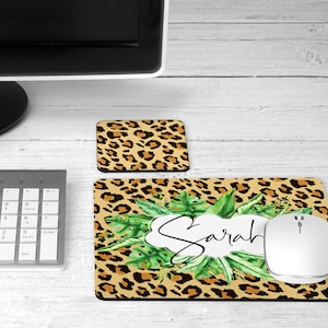 May include: A brown and black leopard print mouse pad with green leaves and the name "Sarah" in a white circle. A white wireless mouse is on the mouse pad.