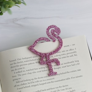 May include: A pink glitter flamingo bookmark is placed on an open book. The book is open to a page with text about a doctor's office.