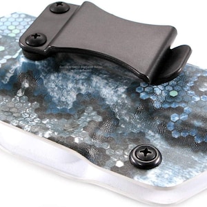 Pu&ograve; includere: Primo piano di una fondina con clip e viti nere. La fondina presenta un motivo esagonale blu, grigio e bianco. Il testo "Custom KYDEX Dig Camo Holsters" &egrave; visibile.