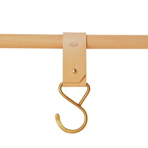 May include: A leather strap with a brass hook hangs from a wooden rod. The strap has the word "Artisan" embossed on it.