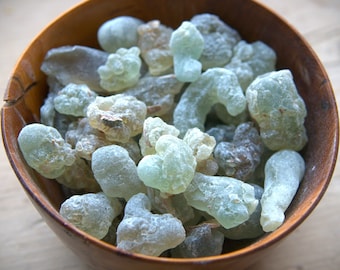 May include: A wooden bowl filled with a variety of pale green and white resin pieces. The resin is translucent and has a slightly powdery texture.