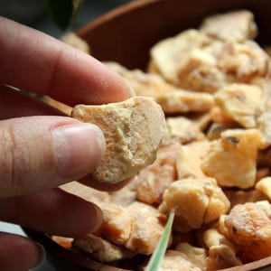 May include: A collection of irregular, light tan and beige resinous chunks with a matte, textured surface. The pieces are varied in size and shape, displaying a natural, earthy appearance with subtle variations in colour ranging from pale yellow to brown.
