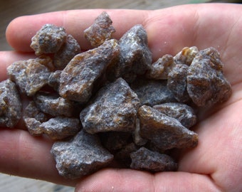 Puede incluir: Primer plano de un puñado de piezas de resina marrón y gris. La resina tiene una forma irregular y una superficie rugosa y texturizada.