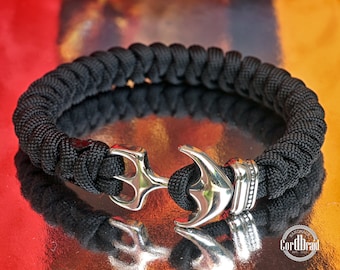 May include: Black paracord bracelet with a silver anchor charm and a silver bead. The bracelet is braided and has a CordThread logo.