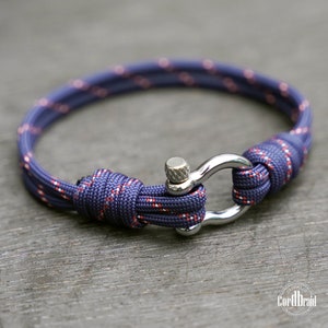 Könnte beinhalten: Ein dunkelblaues und rotes Paracord-Armband mit einem silbernen Verschluss. Das Armband ist aus einem doppelfädigen Paracord gefertigt und hat einen silbernen Verschluss.