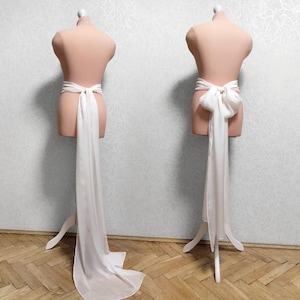 May include: A white satin sash with a long train, tied in a bow at the waist. The sash is displayed on a white mannequin.