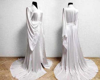Op de afbeelding: Een witte satijnen badjas met lange mouwen en een strikceintuur. De badjas heeft een vloeiende, elegante vorm.
