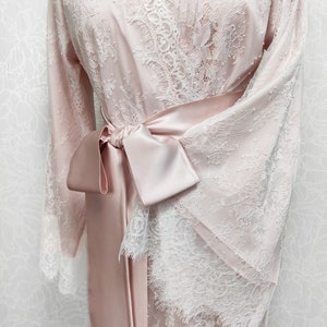 May include: A blush pink satin robe with white lace detailing and a matching satin sash tied at the waist.