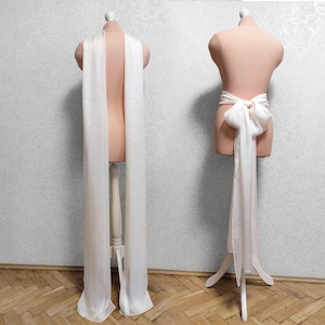 May include: A white satin sash with a large bow at the back. The sash is displayed on a white mannequin.