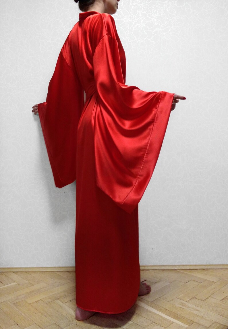 May include: A long, red satin robe with wide sleeves. The robe is tied at the waist with a sash.