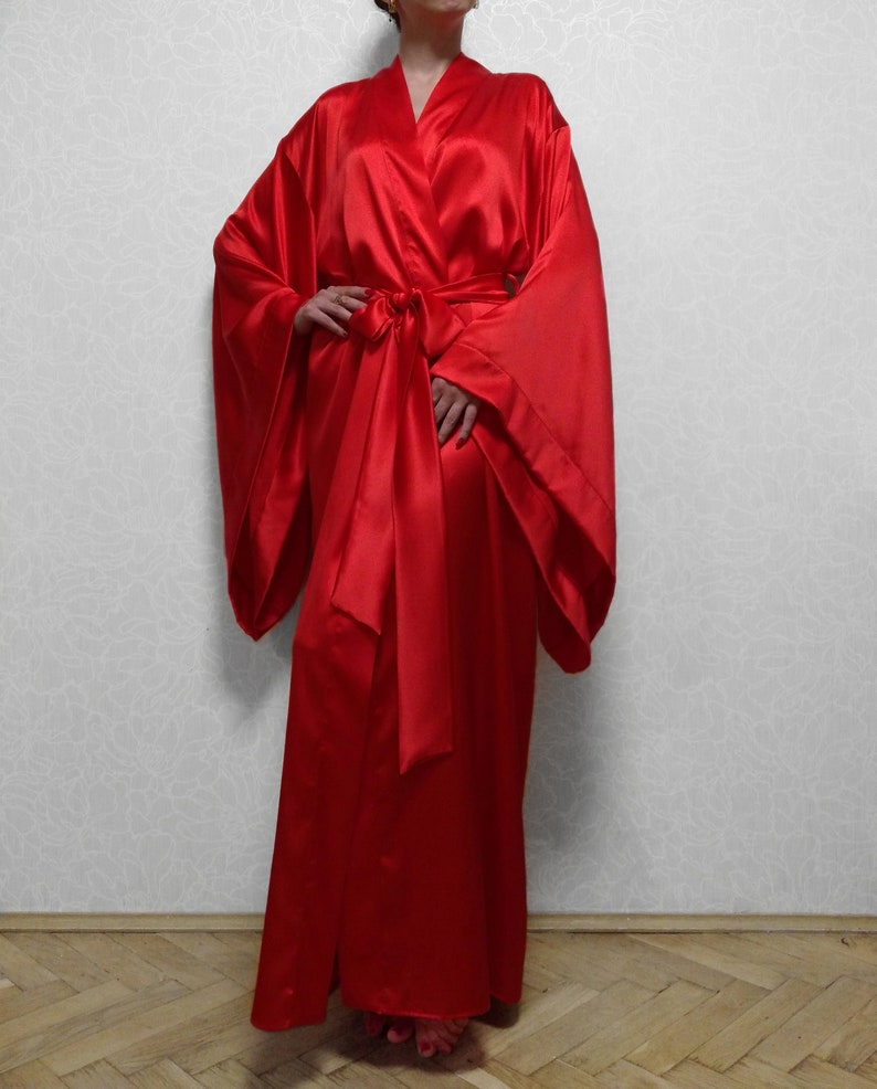 May include: A long, red satin robe with wide sleeves and a sash tie. The robe is floor-length and has a classic kimono style.