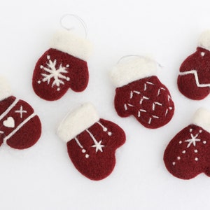 May include: Six felt mitten ornaments in burgundy with white trim and various white embroidered designs, including snowflakes, hearts, and stars.