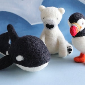 Può includere: Tre giocattoli di animali in feltro: un'orca in bianco e nero, un orso polare bianco e un puffin bianco con becco e piedi arancioni.