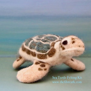 May include: A hand-felted sea turtle kit, featuring a light brown and blue shell with a white body. The turtle is posed walking on a light blue surface. The text "Sea Turtle Felting Kit" and "www.thefibreark.com" is printed below the turtle.