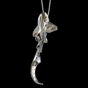 May include: A silver-colored pendant necklace featuring a detailed, three-dimensional sculpture of a shark. The shark is suspended from a silver chain.