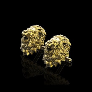 May include: A pair of gold lion head cufflinks. The lion heads are detailed and realistic, with a mane of hair and a fierce expression.