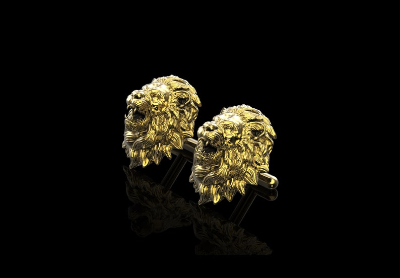 May include: A pair of gold lion head cufflinks. The lion heads are detailed and realistic, with a mane of hair and a fierce expression.