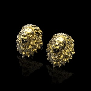 May include: A pair of gold lion head cufflinks. The lion heads are detailed and have a realistic appearance.