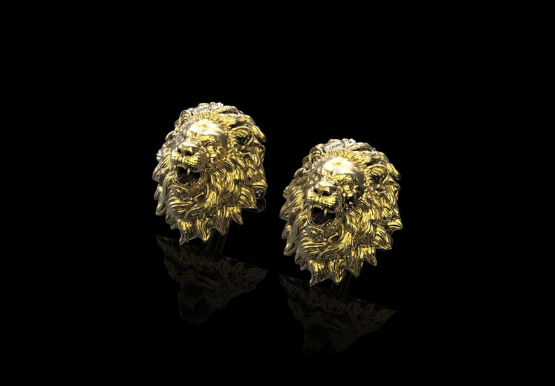 May include: A pair of gold lion head cufflinks. The lion heads are detailed and have a realistic appearance.