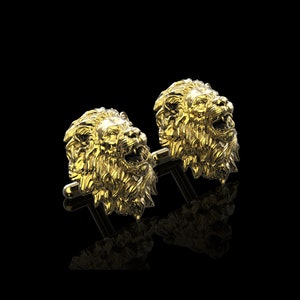 May include: A pair of gold lion head cufflinks. The lion heads are detailed and realistic, with a textured mane and open mouths.